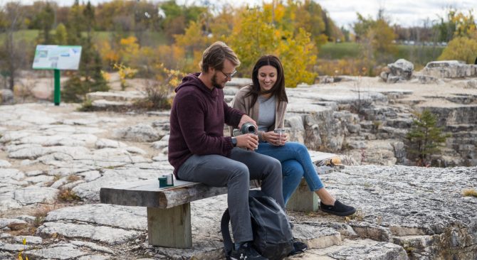 Two people sitting at Quarry Park on a fall day, pouring coffee into a thermos