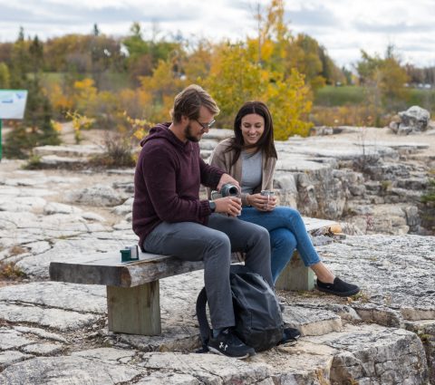 Two people sitting at Quarry Park on a fall day, pouring coffee into a thermos