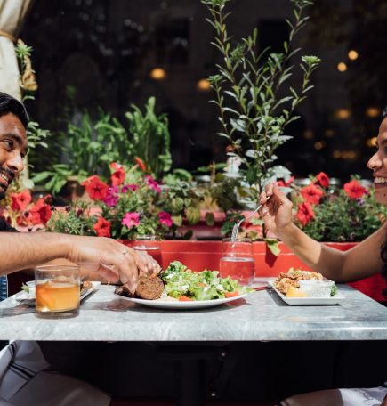 Two people share food on an outdoor patio, in front of a red-framed window at The Peasant Cookery in The Exchange District.