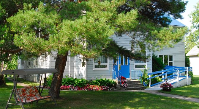 Exterior view of a grey house with a light blue door with a tree in the yard at The Staff House B&B.