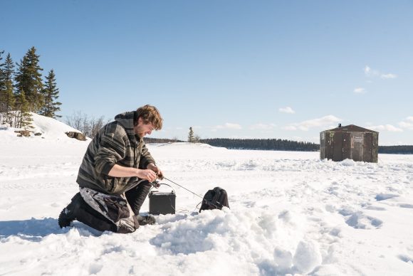 Atravesando el hielo con un sedal en un soleado día de invierno.