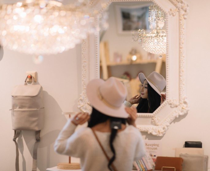 A woman tries on a floppy-brimmed hat in front of a mirror