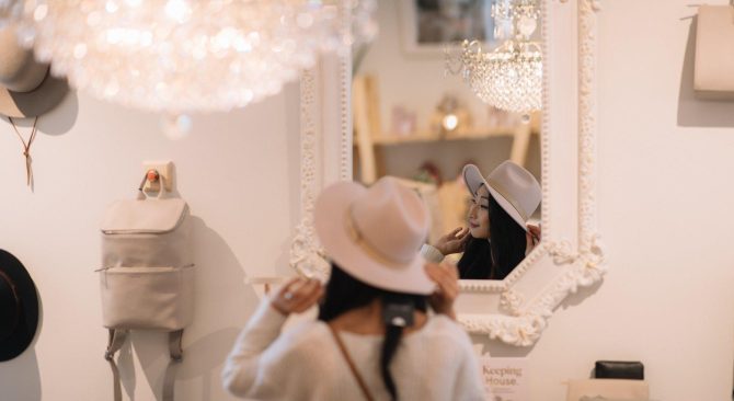 A woman tries on a floppy-brimmed hat in front of a mirror