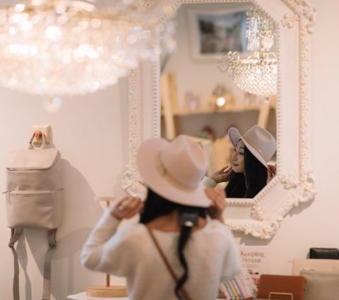 Une femme essaie un chapeau à bords flottants devant un miroir.