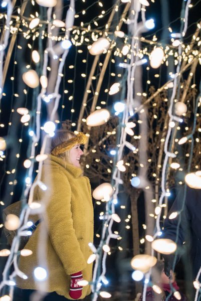Une femme emmitouflée dans son manteau, son chapeau et ses moufles admire les lumières éclatantes.
