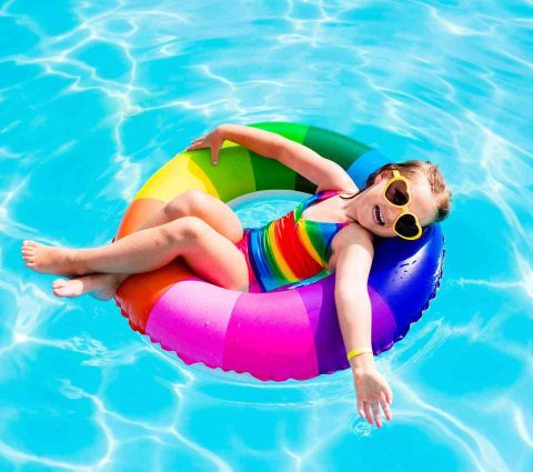 A child wearing heart-shaped sunglasses floating in a pool on a rainbow coloured inner tube.
