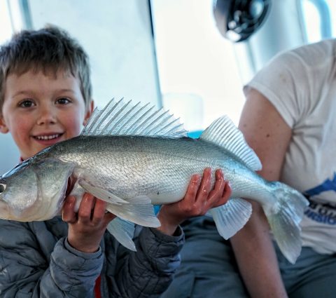 A child holds up their walleye caught while ice fishing.