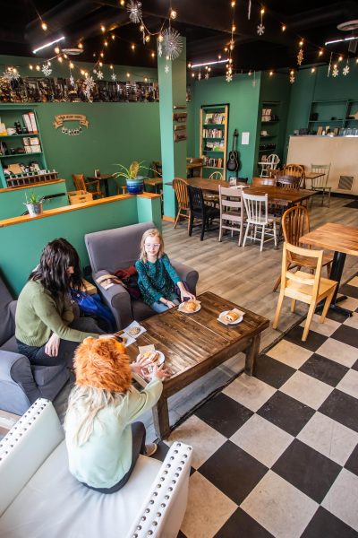 Mother and two daughters sit in a cozy cafe at a low table. The walls are teal, the floor is black and white tile.