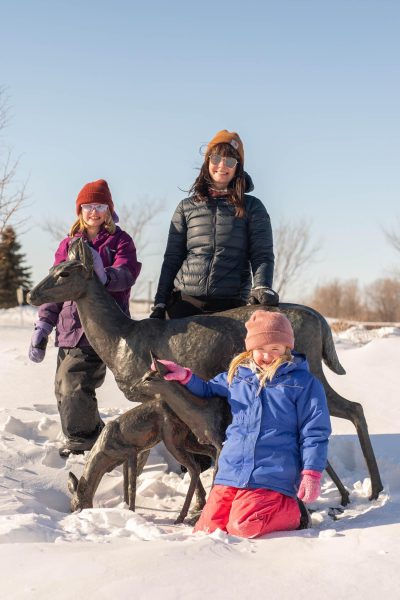 Exterior shot of mother and two daughters in the snow posing with the metal deer statues.