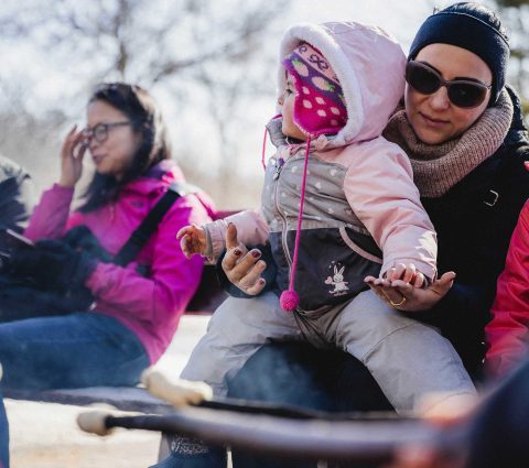 A family sitting around a firepit roasting marshmallows after a day of tobogganing.