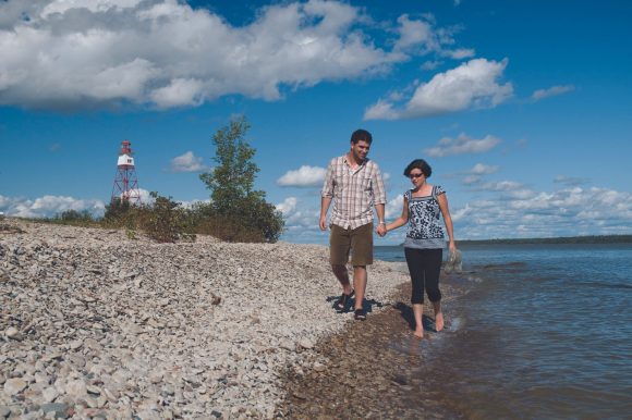 Deux personnes se tenant par la main, marchant sur la plage rocheuse au bord de l'eau.