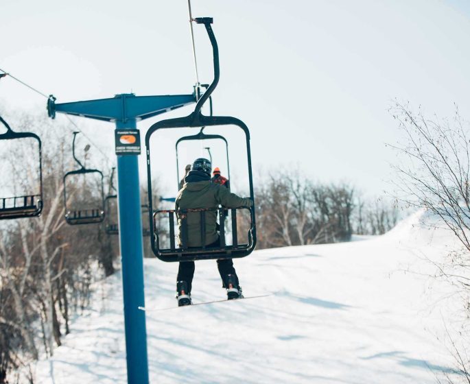 Un snowboarder monte en télésiège sur la pente enneigée de Holiday Mountain.