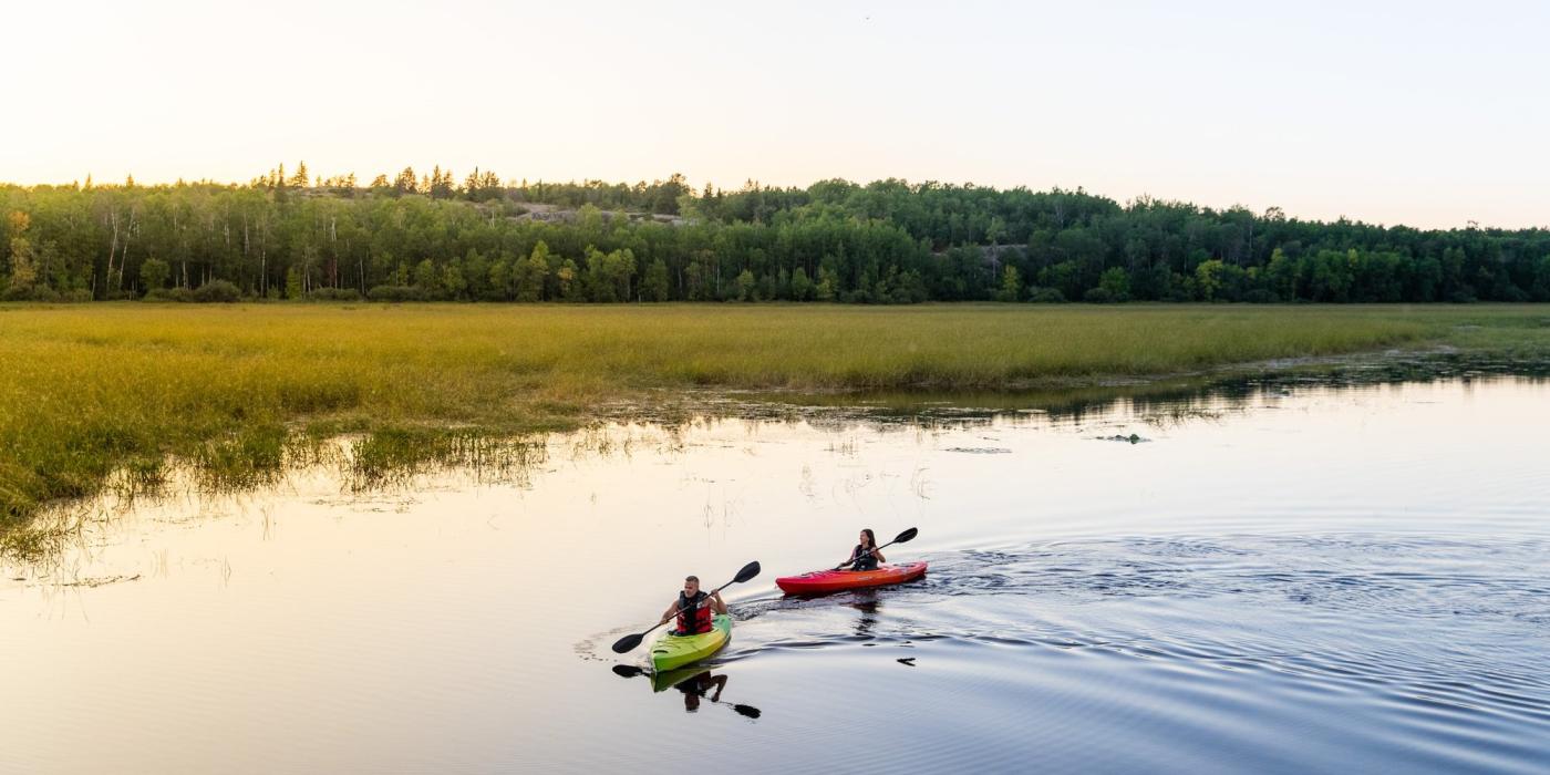 Dos kayakistas se deslizan por un lago tranquilo al atardecer.