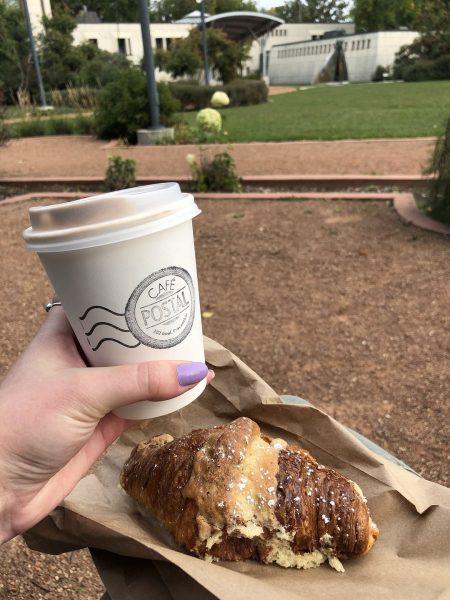Alguien sostiene un café y un cruasán del Café Postale de San Bonifacio.