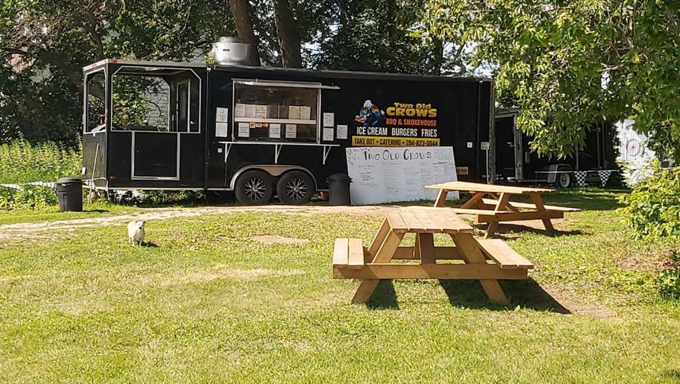 Zwei Picknicktische vor dem Two Old Crows BBQ Food Truck.