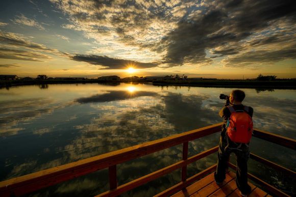 Une personne se tenant sur la promenade et prenant une photo du coucher de soleil.