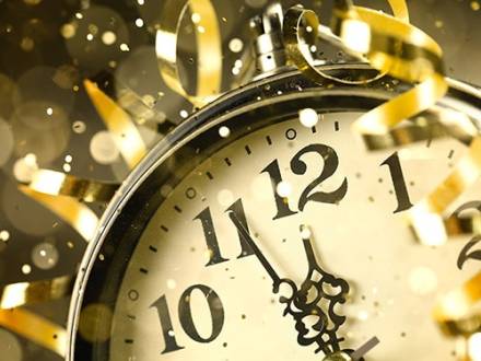 Vintage clock showing a few minutes to midnight surrounded by gold streamers and soft glowing festive lights.