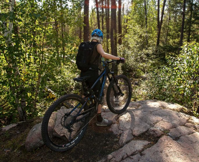Isang taong nagmo-mountain biking sa kagubatan na naliliwanagan ng araw sa Whiteshell Provincial Park.