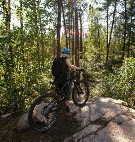 A person mountain biking through the sunlit forest in Whiteshell Provincial Park.