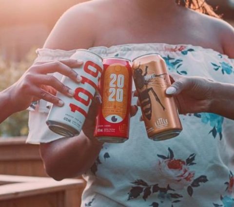 Trois personnes applaudissent avec trois canettes différentes de la bière Little Brown Jug, brassée à Winnipeg.
